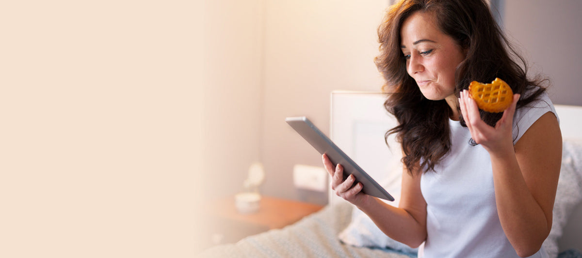 woman eating in bed watching her phone